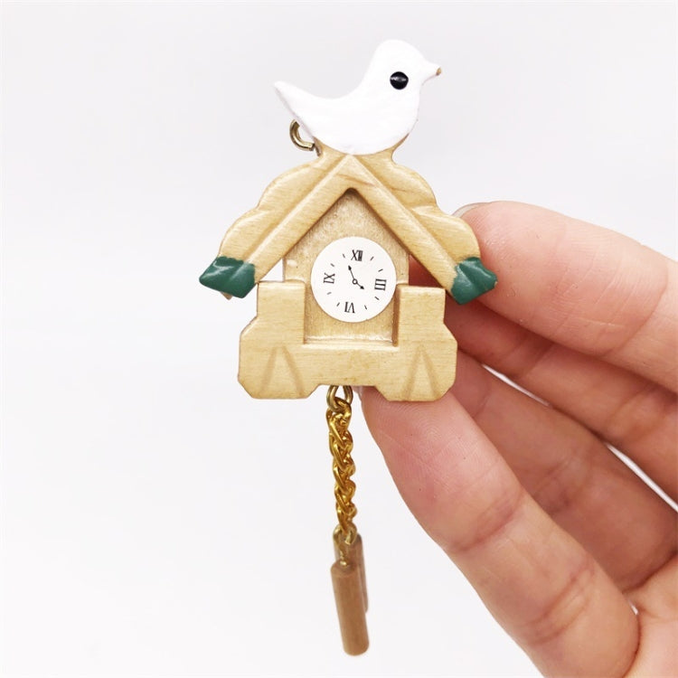 Mini birdhouse clock on gold chain with white bird top and round clock face, held by fingers