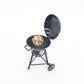 Mini round outdoor oven toy with food on wire grate, open lid, black metal