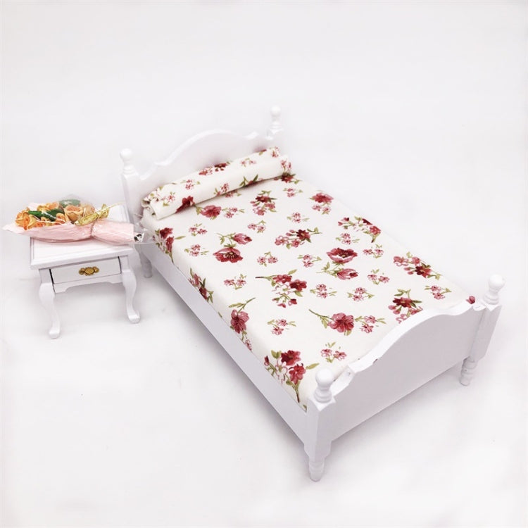 Miniature white single bed with floral bedding and pillow, angled top view