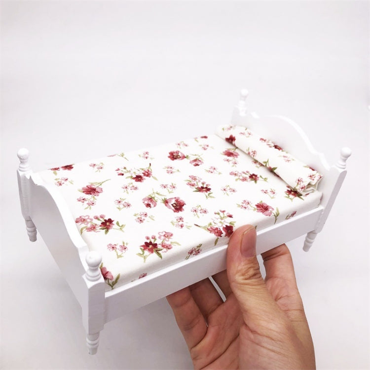 Miniature white single bed with floral mattress; hand shows scale