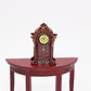 Mini vintage toy clock on red round tabletop, yellow face with Roman numerals and pendulum knob