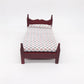 Front view of mini dollhouse single bed toy with dark maroon frame and patterned white bedding