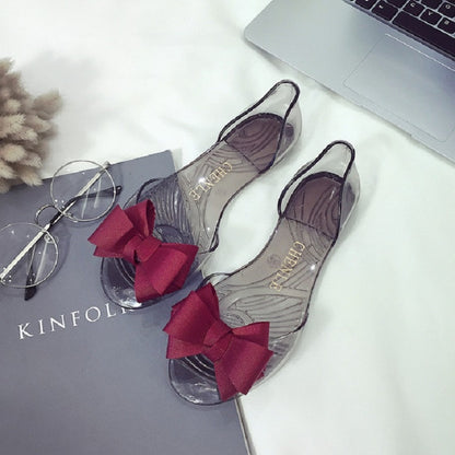 Transparent jelly flat shoes with red bow accents and open toe design