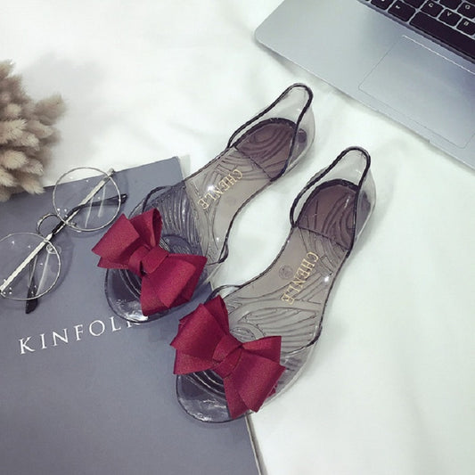 Transparent jelly flat shoes with red bow accents and open toe design
