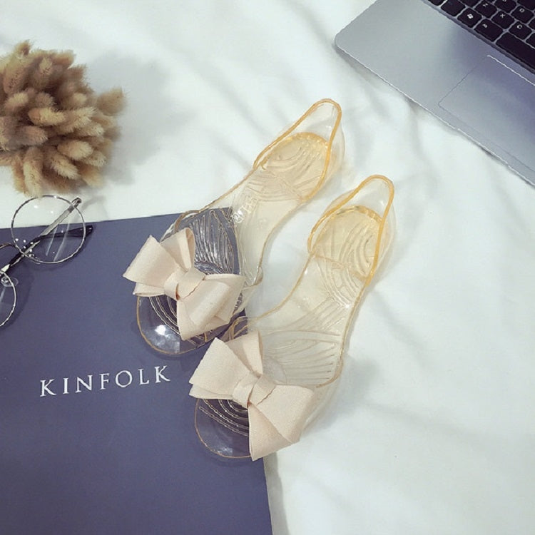 Transparent flat jelly shoes featuring a cream bow detail and open toe