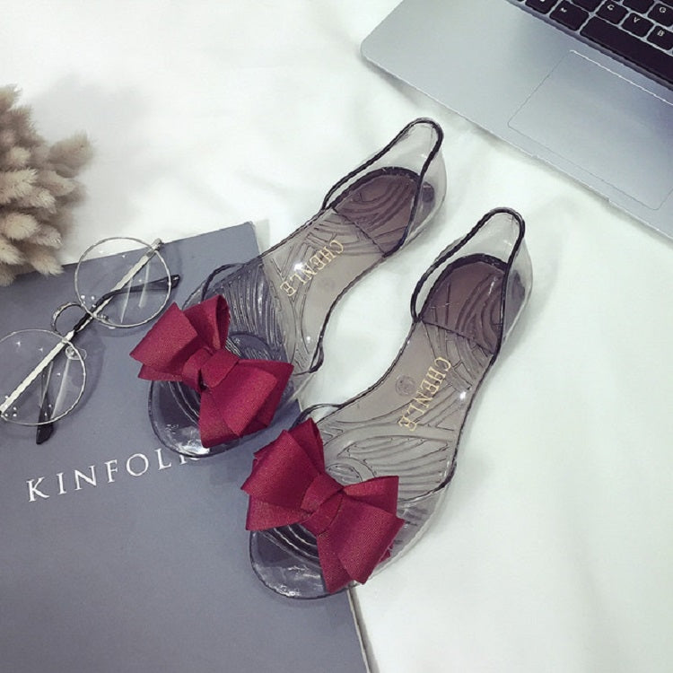 Transparent flat jelly shoes featuring a dark red bow detail and open toe