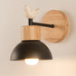 Wall-mounted bird accent lamp with round wood backplate, black dome shade, lit bulb
