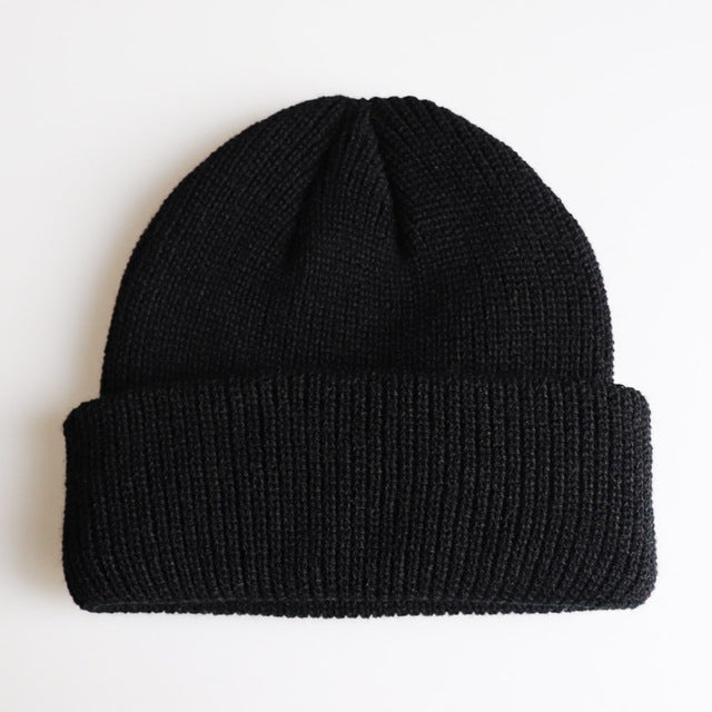 Black ribbed knit beanie with folded cuff and small top knot detail