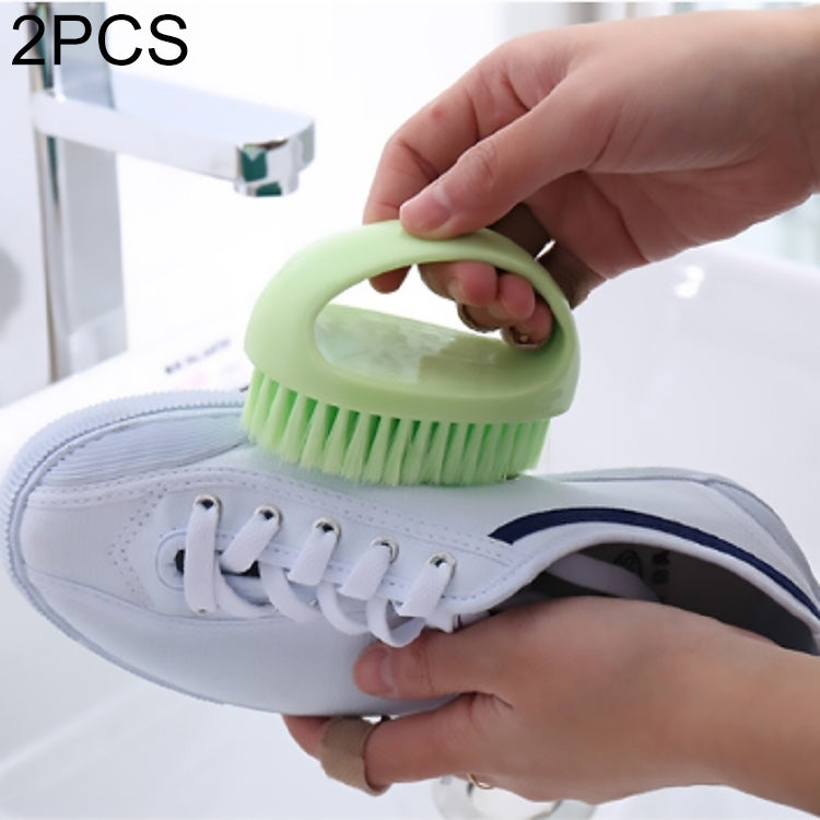 Green handheld cleaning brush scrubbing a white sneaker on a sink area