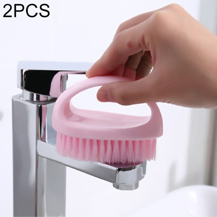 Pink handheld cleaning brush with bristles rinsed under a faucet