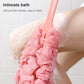 Pink long-handle bath brush scrubbing on skin with fluffy mesh head