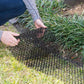 Black wire mesh barrier mat being installed with hands in grass