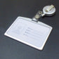 Retractable badge reel with clear card holder and metal clip attached to dark surface
