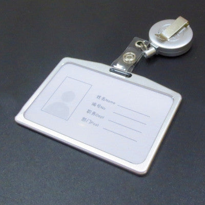 Retractable badge reel with clear card holder and metal clip attached to dark surface