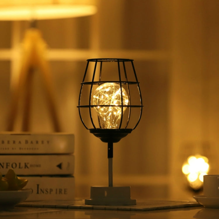 Wire cage LED table lamp with warm glowing light inside, centered on a base