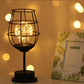 Wire cage LED table lamp with warm glow beside a framed photo on a side surface