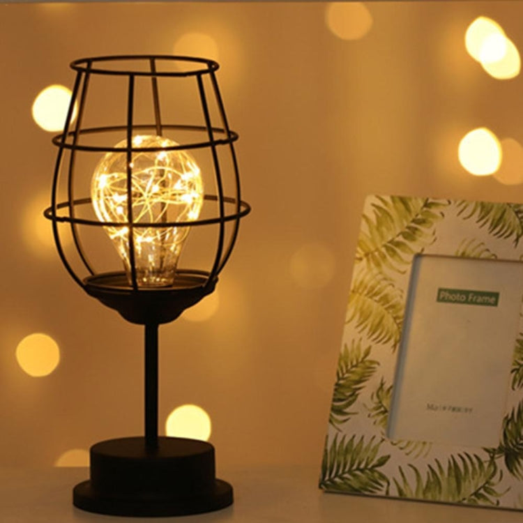 Wire cage LED table lamp with warm glow beside a framed photo on a side surface