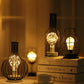 Bottle-shaped LED table lamp and wire cage LED lamp glowing on a side table