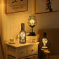 Bottle and wire cage LED table lamps glowing together on a cabinet and side table