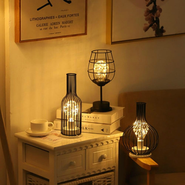 Bottle and wire cage LED table lamps glowing together on a cabinet and side table