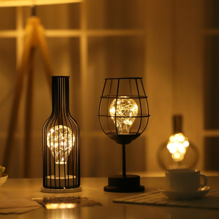 Two bottle-style LED table lamps on a table, warm light from metal cages