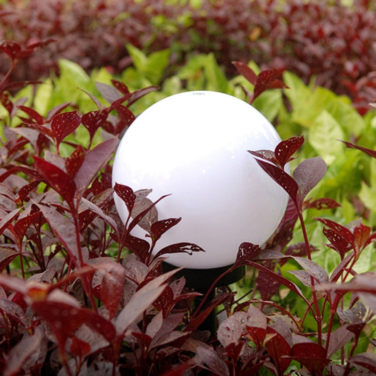 Solar ground light bulb with round white globe, surrounded by red and green plants