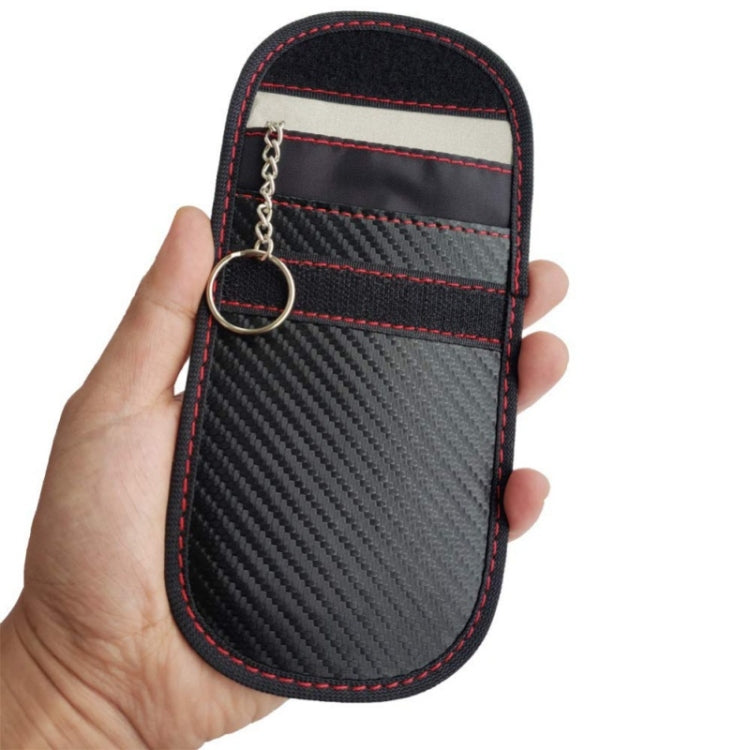 RFID key fob shielding pouch close-up, carbon-fiber fabric with red stitching and metal keyring