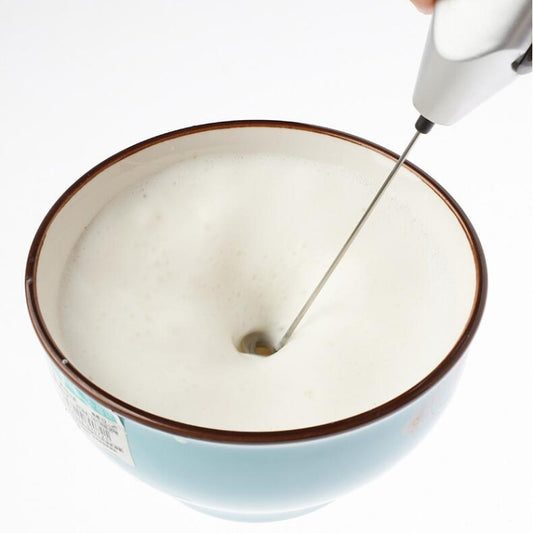 Handheld egg beater whisk inserted into a bowl of smooth white mixture