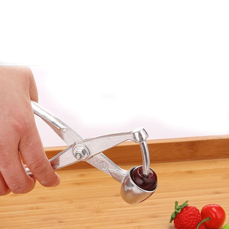 Hand holding stainless steel cherry corer cutting into a cherry on a wooden surface
