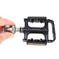 Hand pulling a quick-release axle from a black bike pedal with orange reflector strip