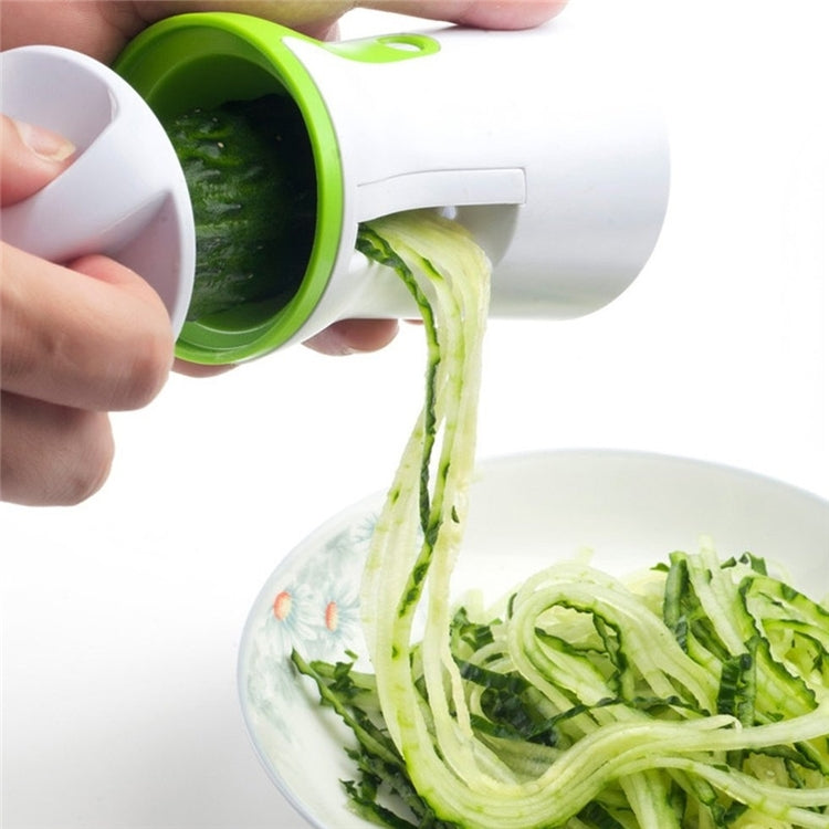 Hands feeding cucumber into a green spiral grater, shredded strands falling out.