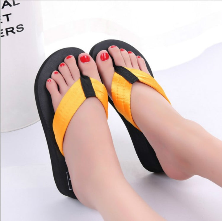 Orange wedge flip-flops with black thong strap, worn on bare feet