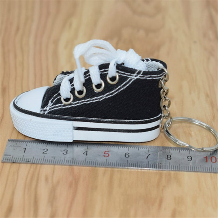 Black mini canvas sneaker keychain beside a small ruler for size reference