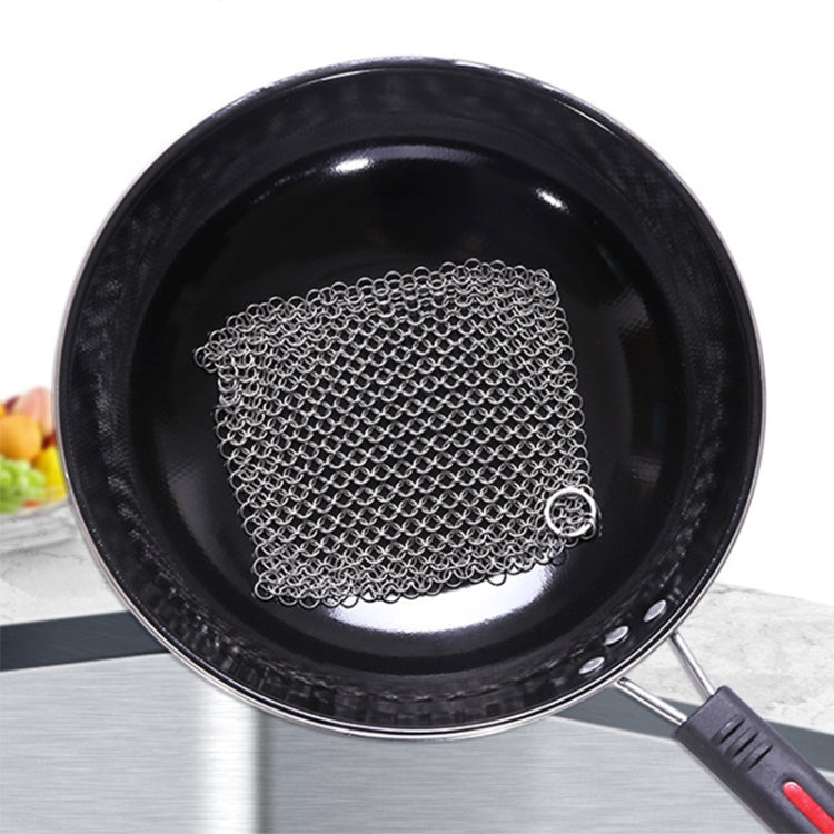 Square stainless steel mesh pot scrubber pad with metal ring handle, used on pan
