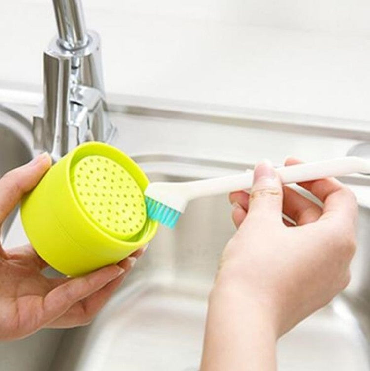 Hands using a teal-bristle cleaning cup brush on a sink edge gap
