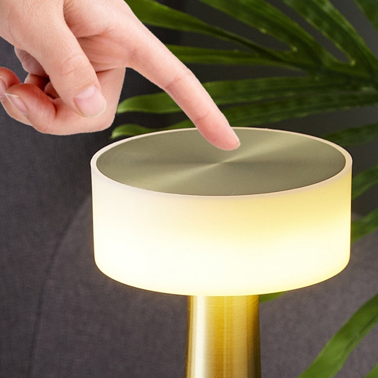 LED table lamp with gold base and glowing white shade, hand pressing top