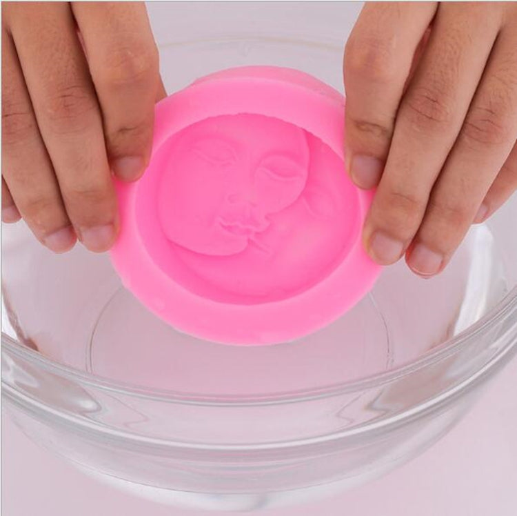 Pink silicone face mold held by hands, showing embossed baby-face cavity.