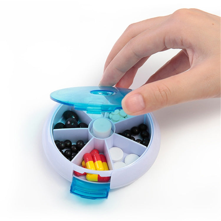 Blue rotating plastic pill box opened to reveal mixed tablets and capsule compartments