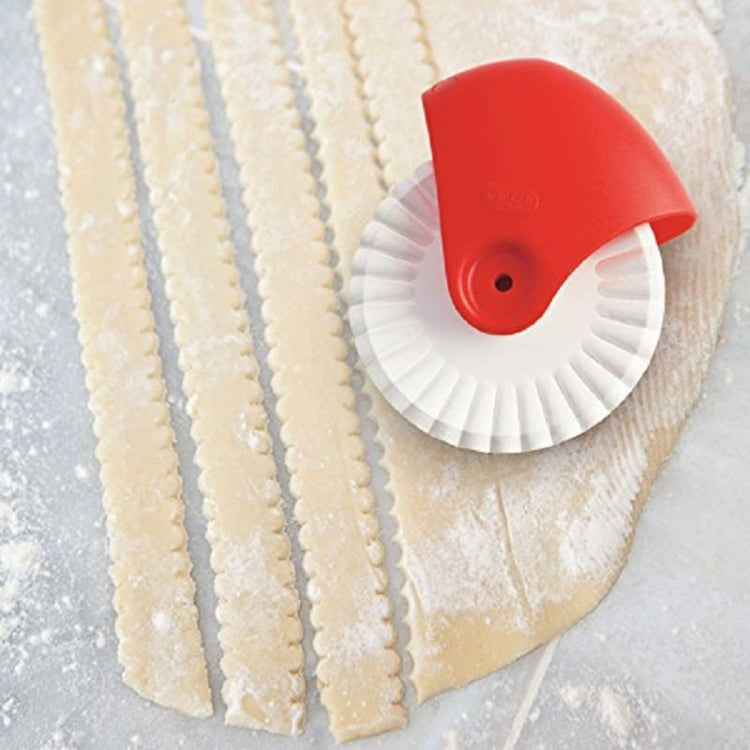 Red pasta cutter wheel rolling along dough strips with white ridged edge