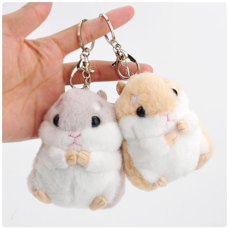 Plush hamster keychain bag pendants held by hand: gray and tan with key rings