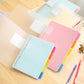Pastel loose-leaf notebooks with spiral binding and colored tab sections, stacked on table