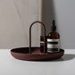 Brown round storage tray with two upright handles, holding a glass bottle.