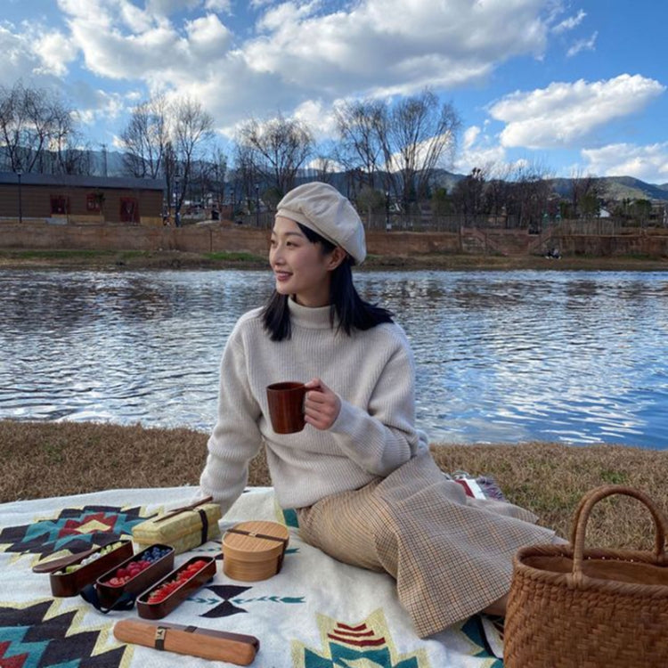 Wood bento lunch box with lid on picnic setup beside tableware