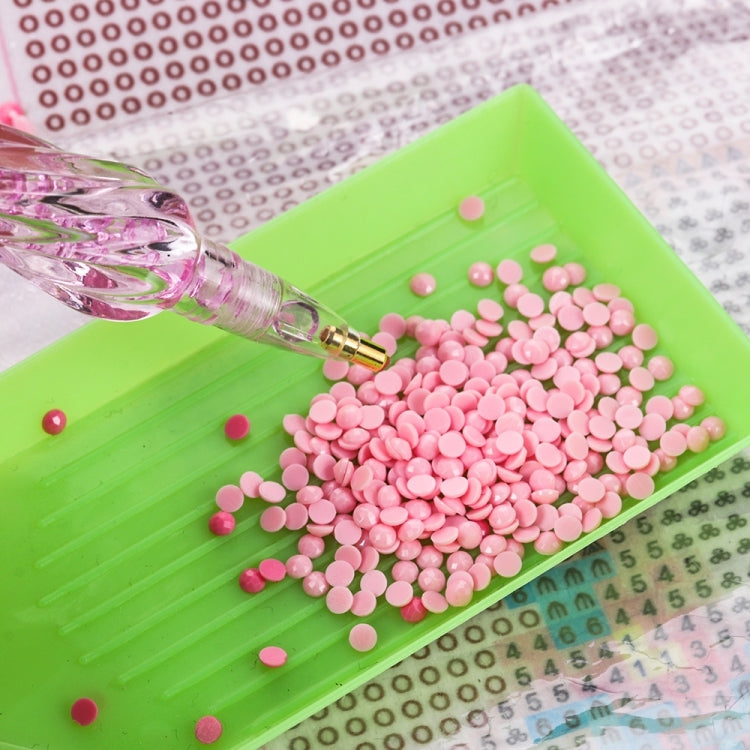Pink diamond painting pen beside pink rhinestone beads on green tray