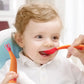 Baby learning-to-eat spoon and fork set held with red scoop and orange handles