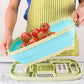 Folding plastic cutting board with blue tray being lifted, holding tomatoes and peppers