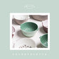 Green plastic vegetable drain basket among pastel bowls