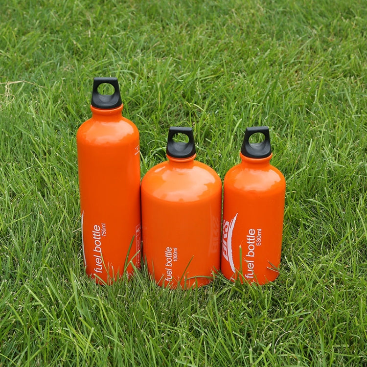 Three orange fuel bottles standing on grass, black caps with carry loops.