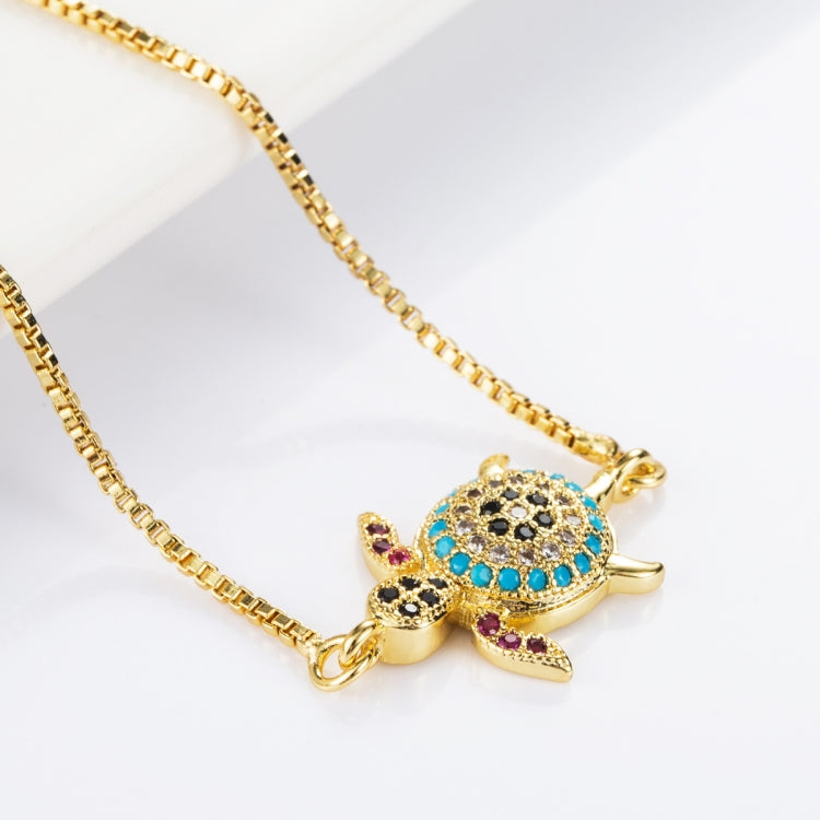 Gold-tone chain bracelet with turtle charm, blue center and black with pink stone accents