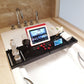 Retractable bathtub shelf rack with black trays, glassware, and tablet display